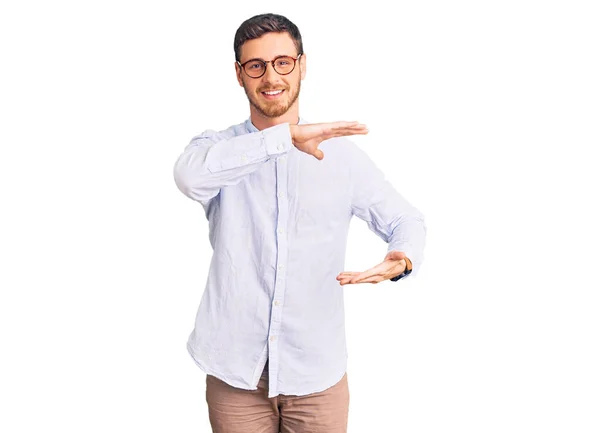英俊的年轻人 身穿典雅的商务衬衫 戴着一副眼镜 手拿着大号和大号的手势和尺寸符号 微笑着看着摄像机 计量概念 — 图库照片