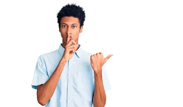 若いアフリカ系アメリカ人の男性がカジュアルな服を着て 唇に手で側に指して指で静かになるように求めている 沈黙と秘密の概念 — ストック写真