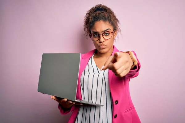 African american business woman wearing glasses working using laptop over pink background pointing with finger to the camera and to you, hand sign, positive and confident gesture from the front