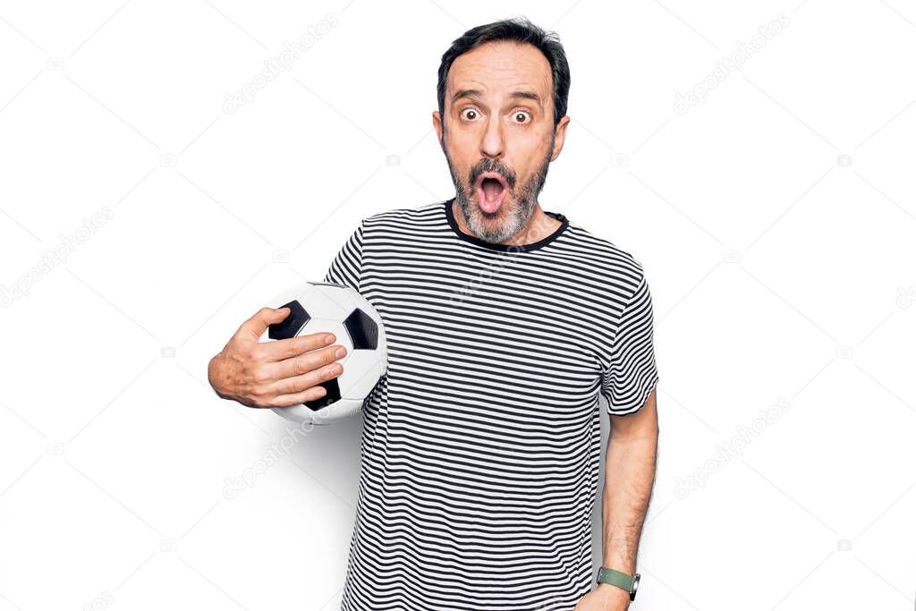 Middle age handsome player man playing soccer holding football ball over white background scared and amazed with open mouth for surprise, disbelief face