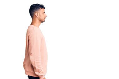 Latin kökenli genç bir adam günlük giysiler giyiyor, rahat bir görünüm takınıyor, doğal bir yüz ifadesi ve kendinden emin bir gülümsemeyle poz veriyor.. 