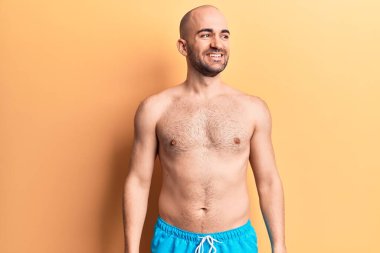 Yüzünde mayo olmayan yakışıklı kel bir adam yan bakıyor, rahat bir görünüm takınıyor ve kendine güvenen bir gülümseme takınıyor.. 