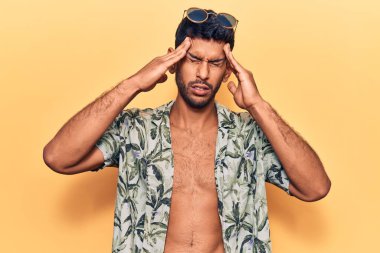 Yazlık tişört giyen, güneş gözlüklü, eli başında genç bir adam. Stres yüzünden baş ağrısı çekiyor. migren ağrısı. 