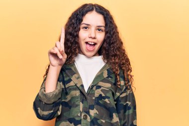 Kıvırcık saçlı, kamuflaj ceket giyen güzel bir kız çocuğu başarılı bir fikirle işaret ediyor. Heyecanlı ve mutlu. Bir numara.. 