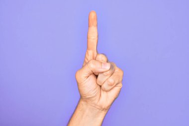 İzole edilmiş mor arka planda parmaklarını gösteren beyaz bir gencin eli işaret parmağı kullanarak bir numarayı sayıyor, fikir ve anlayış gösteriyor.