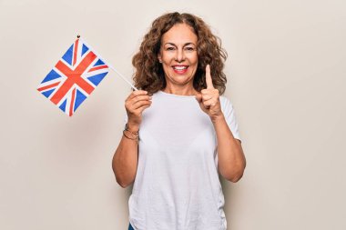 Orta yaşlı, güzel bir turist kadın, izole edilmiş beyaz arka planda Birleşik Krallık bayrağını tutuyor. Bir fikir veya soru işareti ile gülümsüyor.