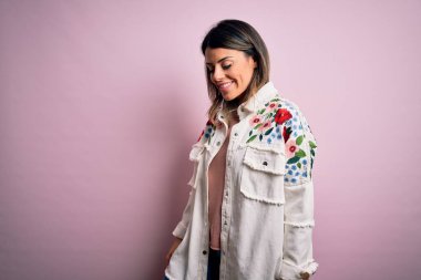 Moda kıyafetleri giyen genç ve güzel bir kadın. Manken, sokak tarzı giyiniyor. Pembe arka planda dikiliyor.