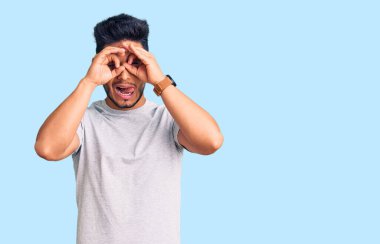 Yakışıklı Latin Amerikalı genç adam sıradan bir tişört giyiyordu. Dürbün gibi güzel hareketler yapıyordu. Gözleri parmaklarından dışarı bakıyordu. çılgın ifade. 