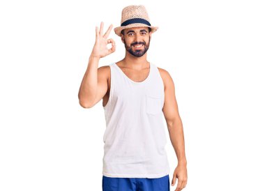 Gündelik yaz şapkası takan genç İspanyol adam olumlu gülümsüyor ve el ve parmaklarıyla 