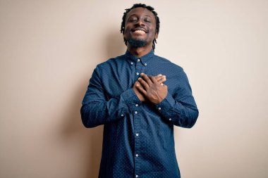Genç, yakışıklı, Afro-Amerikalı bir adam beyaz arka plan üzerinde dikilmiş elleri göğsünde, gözleri kapalı ve yüzünde minnet dolu bir jest ile gülümsüyor. Sağlık kavramı.
