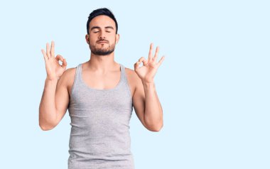 Mayolu ve kolsuz tişörtlü genç yakışıklı adam rahatlamış ve gözleri kapalı gülümsüyor parmaklarıyla meditasyon hareketi yapıyor. yoga konsepti. 