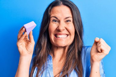 Genç, güzel esmer kadın makyaj yapıyor. Mavi arka planda sünger kullanıyor. Gururla bağırıyor, zaferi kutluyor.