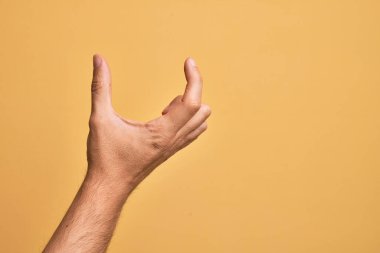 İzole edilmiş sarı arka plan üzerinde parmaklarını gösteren beyaz bir adamın eli. Görünmez bir şeyi alıp, parmaklarıyla uzayı gösteren bir nesneyi tutuyor.