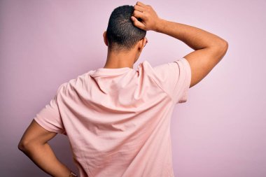 Yakışıklı Afro-Amerikalı adam, günlük tişört ve pembe arka planda gözlük takıyor. Geriye doğru, şüpheyi kafa kafaya düşünüyor.