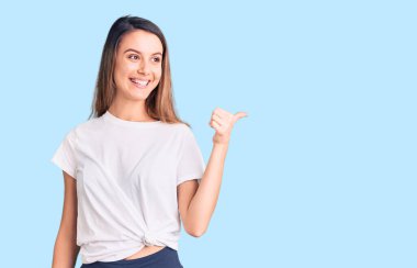 Gündelik tişört giyen, gülümseyen, gülümseyen, gülümseyen ve baş parmağıyla yan tarafı gösteren güzel bir kız.. 