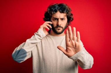 Sakallı yakışıklı bir adam kırmızı arka planda akıllı telefonla konuşuyor. Dur işareti yapıyor. Ciddi ve kendinden emin bir ifadeyle, savunma jesti.