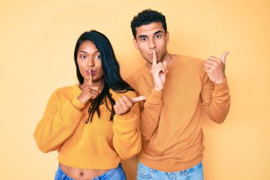 Güzel, Latin, genç bir çift, günlük giysiler içinde sessiz olmak istiyorlar. Parmakları dudaklarında, elleri yana doğru işaret ediyorlar. sessizlik ve gizli konsept. 