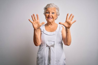 Son sınıf güzeli, gri saçlı kadın beyaz arka plan üzerine yazlık elbiseler giyiyor ve parmaklarını on numarayı göstererek gülümsüyor..