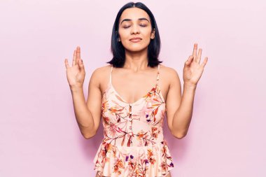 Genç ve güzel Latin kadın günlük kıyafetler giyip rahatlıyor ve gözleri kapalı gülümsüyor parmaklarıyla meditasyon hareketi yapıyor. yoga konsepti. 