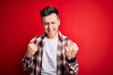 Kırmızı izole arka plan üzerine gündelik modern tişört giyen yakışıklı beyaz adam kolları havada ve gözleri kapalı olarak başarının şaşkınlığını ve şaşkınlığını yaşıyor. Kazanan konsept.