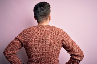 Pembe izole bir arka plan üzerine sıradan bir kazak giyen yakışıklı beyaz bir adam kolları vücudunda geriye doğru bakıyor.