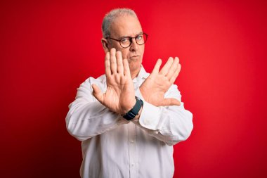 Orta yaşlı yakışıklı, beyaz gömlekli ve kırmızı arka planda gözlüklü adam. Reddedilmiş yüz ifadesi.