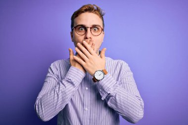 Mor arkaplan üzerine gündelik gömlek ve gözlük takan genç, kızıl saçlı adam ağzı yanlışlıkla ellerle kapatarak şok etti. Gizli konsept.