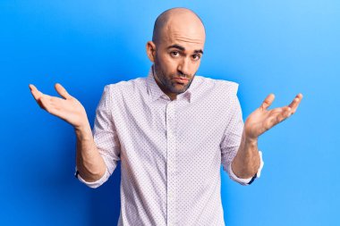 Zarif tişört giyen yakışıklı kel adam habersiz ve kolları açık, hiçbir fikrim yok ve şüpheli bir yüzüm var.. 