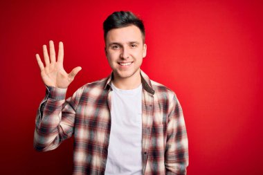 Kırmızı izole edilmiş arka plan üzerine gündelik modern tişört giyen yakışıklı beyaz adam beş numarayı gösterirken kendine güvenen ve mutlu bir şekilde gülümsüyor..