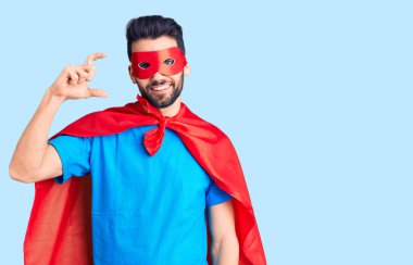 Sakallı, süper kahraman kostümü giyen, kendine güvenen, el hareketi yapan, parmaklarıyla işaret yapan ve kameraya bakan yakışıklı bir genç. ölçüm kavramı. 