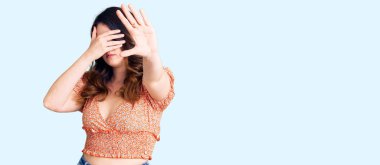 Güzel, genç, esmer, günlük kıyafetler giyen, elleriyle gözlerini kapatan üzgün ve korku ifadeleriyle jest yapan bir kadın. utangaç ve olumsuz kavram. 