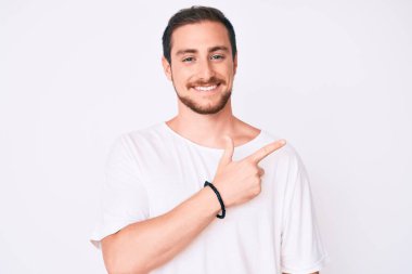 Genç ve yakışıklı bir adam, günlük beyaz tişört giyiyor. Neşeli. Yüzünde mutlu ve doğal bir ifadeyle, elleri ve parmaklarıyla yüzünü gösteren bir gülümseme var. 