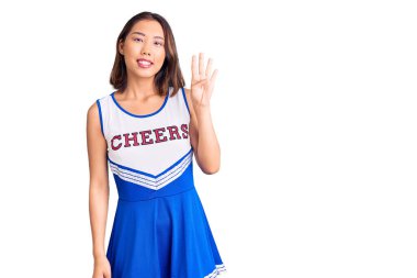 Genç, güzel Çinli kız ponpon kız üniforması giyip dört numarayı gösterip işaret ederken kendinden emin ve mutlu bir şekilde gülümsüyor.. 