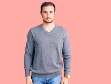 Yüzünde ciddi bir ifade olan günlük kışlık süveter giyen yakışıklı beyaz bir adam. Basit ve doğal bir şekilde kameraya bakıyorsun.. 