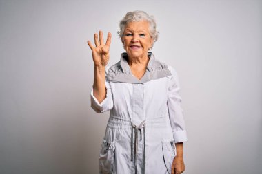 Son sınıf güzeli, gri saçlı, sıradan bir ceket giyen beyaz arka plan üzerinde duran ve parmaklarını dört numarayı gösteren, kendinden emin ve mutlu gülümseyen bir kadın..