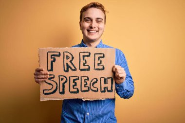 Genç ve yakışıklı kızıl saçlı adam özgürlük istiyor konuşma özgürlüğü mesajı taşıyan afişi tutuyor pozitif ve mutlu görünüyor ve kendine güvenen bir gülümsemeyle dişlerini gösteriyor.