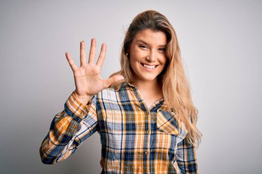 İzole edilmiş beyaz arka plan üzerinde duran ve gülümseyen, kendinden emin ve mutlu gülümseyen genç, sarışın kadın..