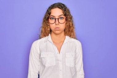 Mavi gözlü, mor arka planda gözlük takan ve komik yüzlü güzel bir kadın. Havayla şişmiş ağız, çılgın bir ifade..