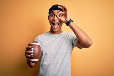 Genç ve yakışıklı Afro-Amerikan adam ragbi topunu izole edilmiş sarı arka planda tutuyordu. Gülümsüyordu. Tamam imzasını atarken parmaklarının arasından bakıyordu.