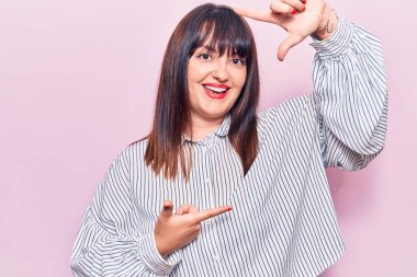 Gündelik kıyafetler giyen, gülümseyen, elleri ve parmakları mutlu yüzlü, çerçeveli genç bir kadın. yaratıcılık ve fotoğrafçılık kavramı. 