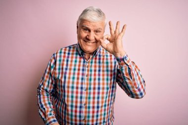 Üst düzey yakışıklı beyaz adam izole edilmiş pembe arka planda sıradan bir tişört giyiyor gülümsüyor ve el ve parmaklarıyla tamam işareti yapıyor. Başarılı ifade.