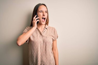 Genç ve güzel bir kadın, beyaz arka plan üzerinden akıllı telefondan konuşuyor kızgın ve öfkeli çığlıklar atıyor, öfkeyle bağırıyor. Öfke ve agresif kavram.