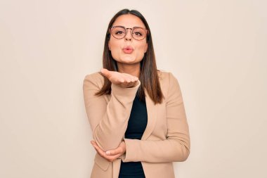 Güzel, esmer, ceketli, beyaz arka planda gözlüklü genç bir iş kadını havada el ele öpüşürken kameraya bakıyor. Güzel ve seksi. Aşk ifadesi.