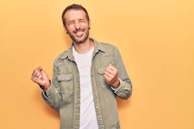 Başarılı olmak için heyecanlı, kolları havada ve gözleri kapalı gülümseyerek zaferi kutlayan gündelik giysiler giyen genç yakışıklı bir adam. Kazanan konsept. 