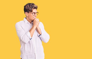 İş kıyafetleri ve gözlük takan genç yakışıklı adam gergin ve heyecanlı, elleri çenesinde yan tarafa bakıyor. 