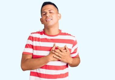 Genç, yakışıklı, sıradan kıyafetler giyen, göğsünde elleri kapalı, yüzünde minnet ifadesi olan Latin bir adam. sağlık kavramı. 