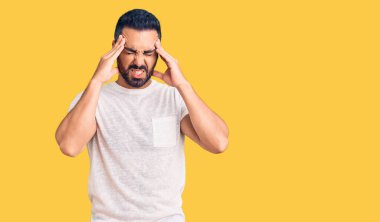 Stres yüzünden başı ağrıyan Latin kökenli genç bir adam günlük kıyafetler giyiyor. migren ağrısı. 