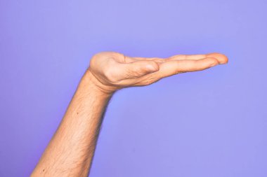 İzole edilmiş mor arka plan üzerinde parmaklarını gösteren beyaz bir gencin eli. Düz avuç içi ürünü sunuyor, el hareketi yapıyor, boş kopya alanı veriyor.