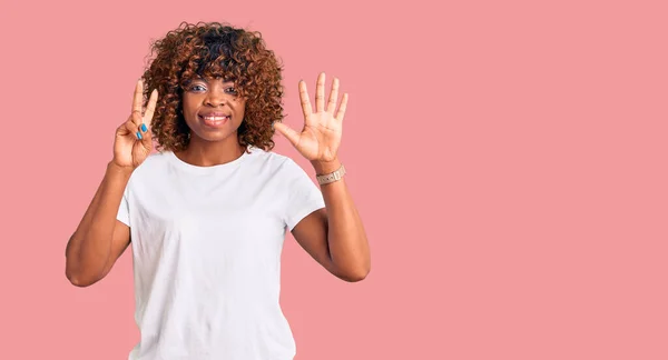 自信と幸せ笑みを浮かべている間若いアフリカ系アメリカ人の女性は カジュアルな白いTシャツを着て指の数7を示すと指摘 — ストック写真