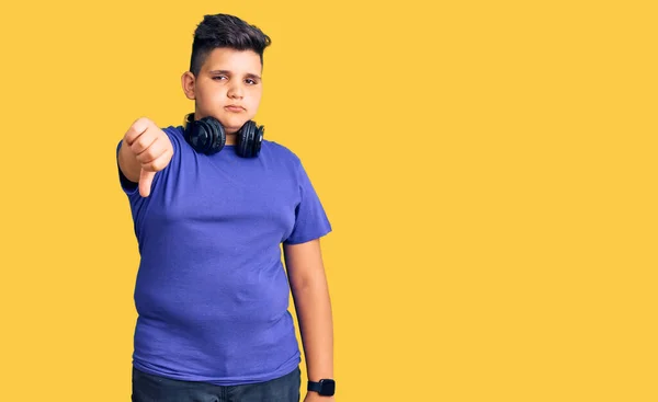 小さな男の子の子供の音楽をヘッドフォンを着て聞いて不満と怒りを示し 親指を下にジェスチャーで否定的に見えます 悪い表現 — ストック写真